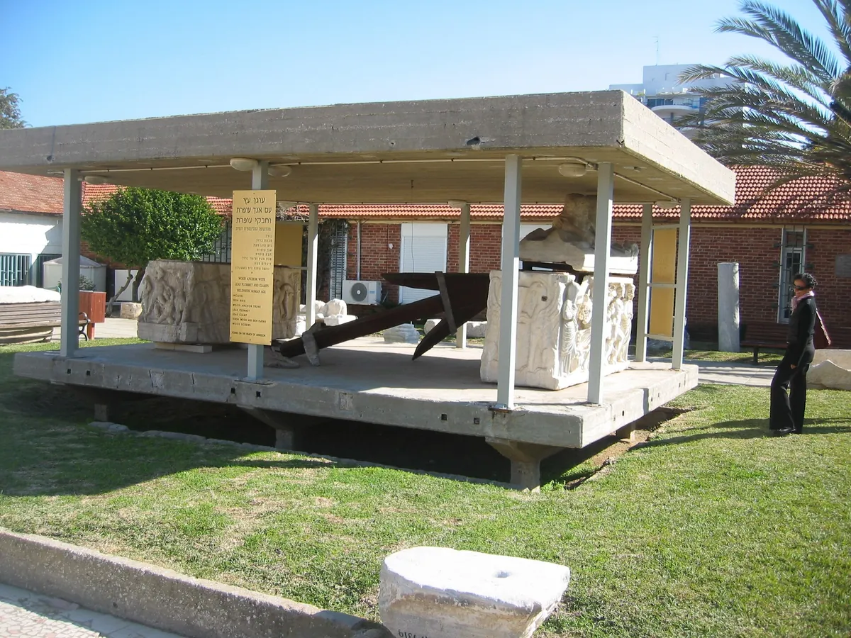 Two Roman sarcophagi and a reconstructed ancient anchor under a canopy in the archaeological garden of Beit HaAm, Afridar
